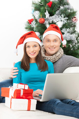 Couple with laptop. Cheerful young couple in Santa hat sitting c