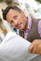 Elegant man reading newspaper on a public bench