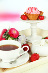 Cup of tea with cakes on wooden tray on table in room
