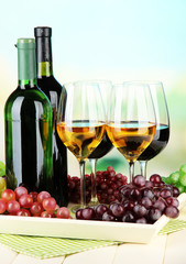 Obraz premium Wine bottles and glasses of wine on tray, on bright background