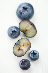 Whole and halved blueberries on white wooden background