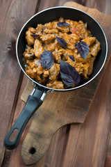 Frying pan with roasted pork on rustic wooden background