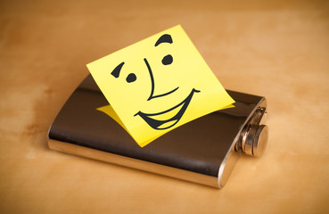 Post-it note with smiley face sticked on a hip flask