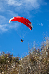 Red paraglider flying in blue sky.