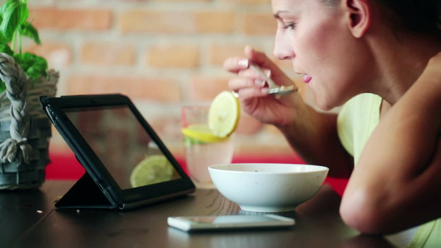 Woman eating soup and using tablet computer in home