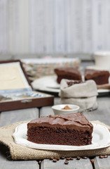 Chocolate cake on white plate, on hessian. Coffee beans on wood
