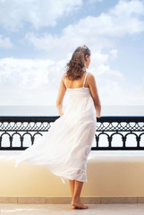Fototapeta na wymiar Back of a young woman in a white dress on a resort background