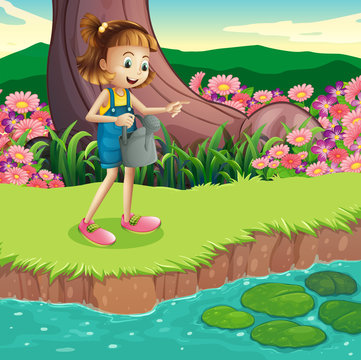 A young girl standing at the riverbank holding a sprinkler