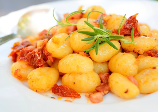 Gnocchi with tomatoes, bacon and onion on the white plate.