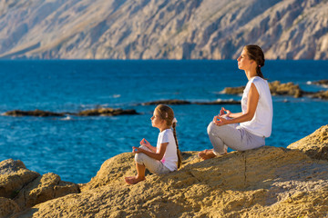 Mother and daughter doing yoga exercise on the beach