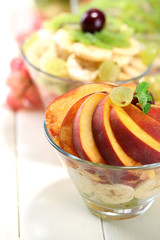 Tasty fruit salad in glass bowls, on white wooden table