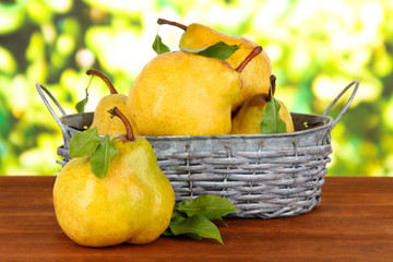 Juicy pears in wicker basket on table on bright background
