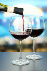 Red wine being poured into wine glass, on bright background