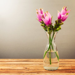Pink tropical flowers in glass vase on wooden table