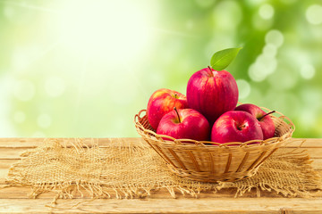 Apples in basket on wooden table over garden bokeh