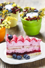Pink layer cake decorated with fresh fruits on wooden table