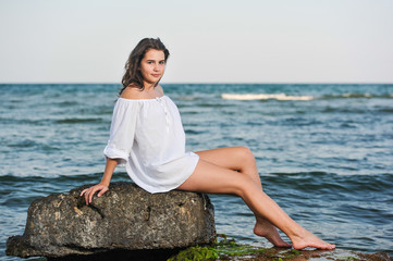 .Teenage girl in white shirt sitting on a rock in the sea 