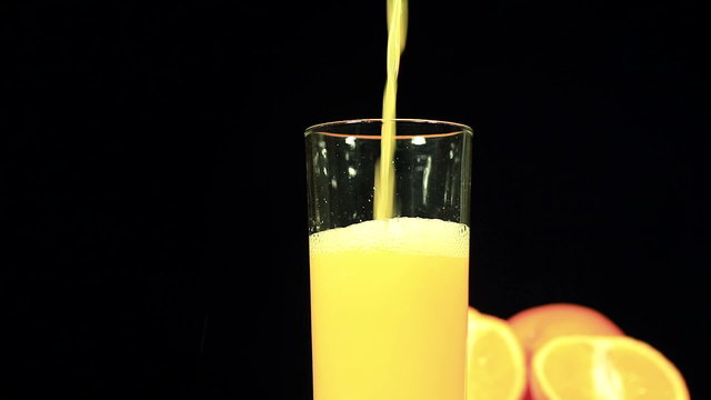 Orange juice flows in  glass on  black background