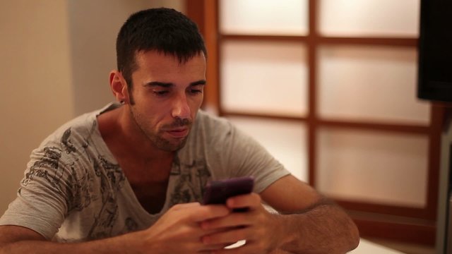 Man texting with his smartphone seated on a bed