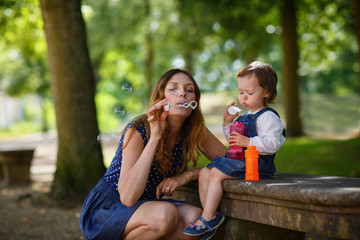 Beautiful mother and little daughter blowing soap bubbles in sum