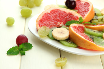 Assortment of sliced fruits on plate, on white wooden table