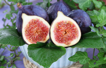 Ripe figs in bowl in leaves on wooden table close-up