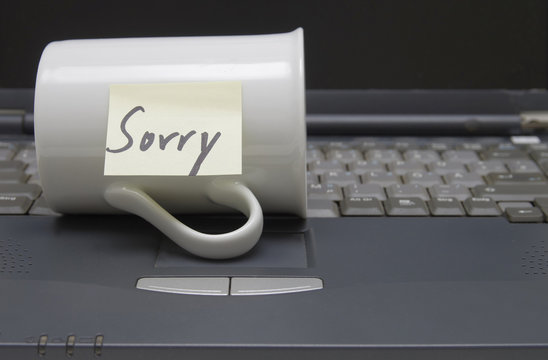 Auf Tastatur liegender Kaffeebecher mit "Sorry"-Noti