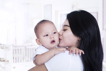 Asian mother kissing her baby at home