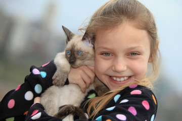 Obraz premium closeup portrait of smiling little girl holding a kitten outdoors and looking at camera