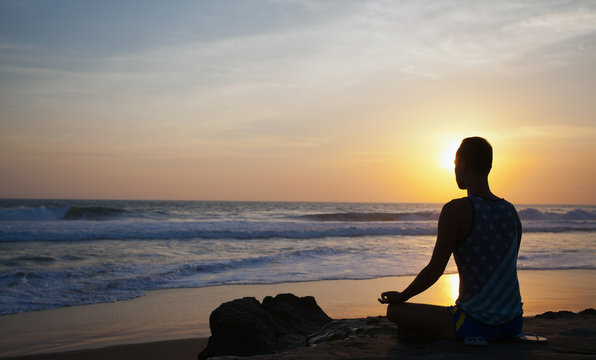 sitting man doing yoga on shore of ocean