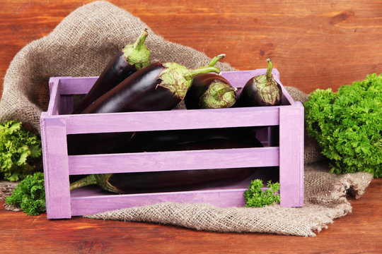 Fresh eggplants in wooden box on table on wooden background