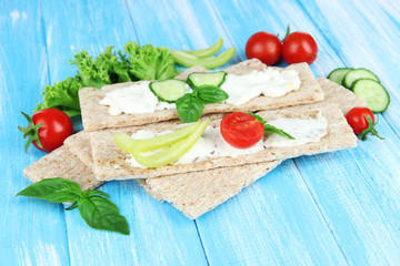 Tasty crispbreads with vegetables on blue wooden background