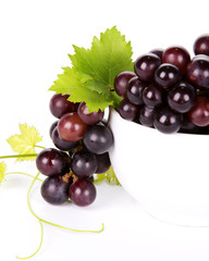 Close-up of branch of black grape in white bowl with leaf