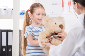 Examining toy. Little girl holding toy bear while doctor examini