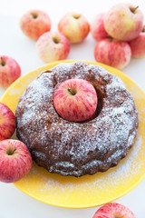 Kugelhopf apple cake on  yellow plate with red apples around