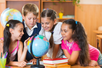 Portrait of cute schoolchildren looking at globe