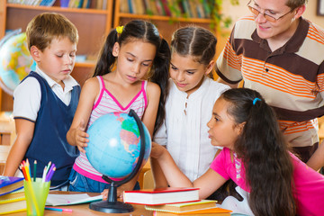 Portrait of pupils looking at globe with their teacher
