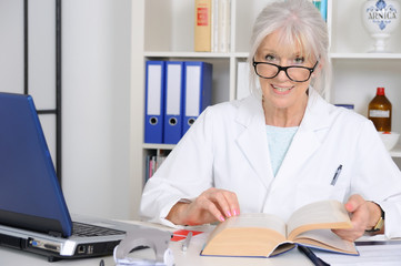 Senior Ärztin schlägt im Fachbuch nach.