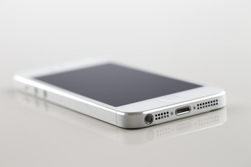 A brand new white smartphone on a white reflective background