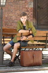 Young handsome man with suitcase waits on bench