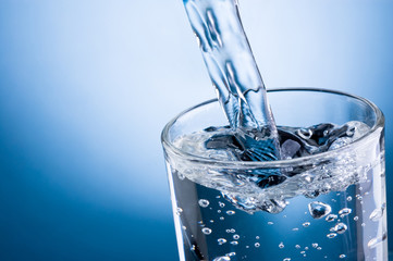 Gießen von Wasser in Glas auf blauem Hintergrund