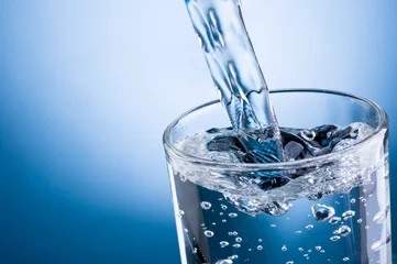 Foto auf Acrylglas Wasser Gießen von Wasser in Glas auf blauem Hintergrund