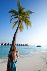 Fototapeta na wymiar Young beautiful woman stands near palm tree, Maldives