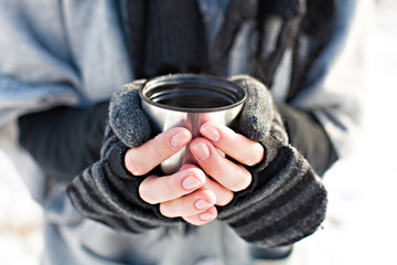 Hands in mittens holding a cup of tea