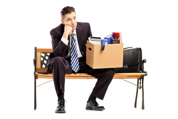 Disappointed businessman in a suit sitting on a bench with a box