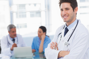 Fototapeta premium Happy doctor looking at camera with colleagues behind