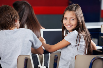 Schoolgirl Holding Digital Tablet At Desk In Classroom