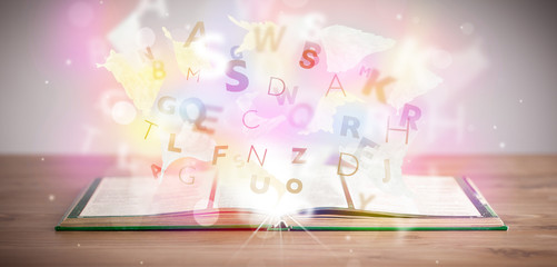 Open book with glowing letters on concrete background