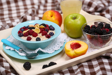 Oatmeal in plate with berries on napkins on wooden tray on bad