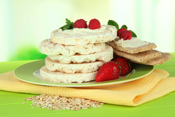 Tasty crispbread with berries on plate, on green table